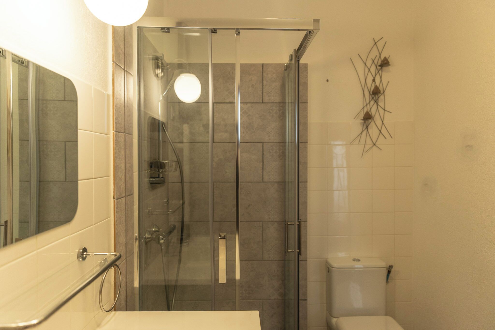 A modern bathroom with a glass-enclosed shower, a toilet, and a sink with a mirror.