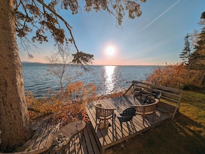 Eine Holzterrasse mit Sitzgelegenheiten und Blick auf ein Gewässer.