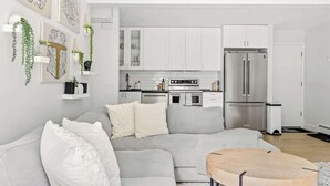 A modern living room with a grey sofa, a wooden coffee table, and a kitchen area with white cabinets and stainless steel appliances. - Bright & Modern | King Suite | Creekside Trail (Boulder)