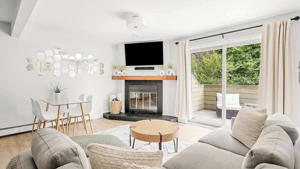 A modern living room with a fireplace, a flat-screen TV, and a dining area with a glass table and chairs. - Bright & Modern | King Suite | Creekside Trail (Boulder)