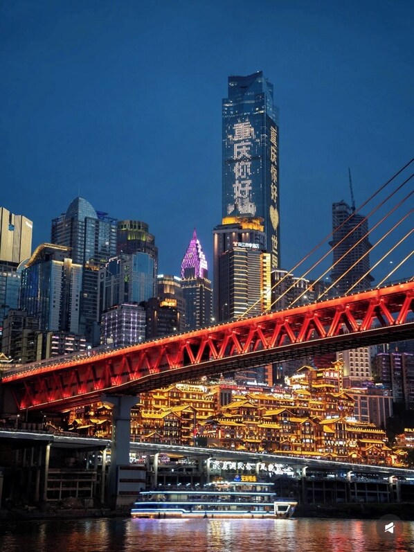A cityscape with a prominent red bridge and illuminated buildings, including a tall skyscraper with vertical lights. - Chongqing Jetbear Hotel (Chongqing)