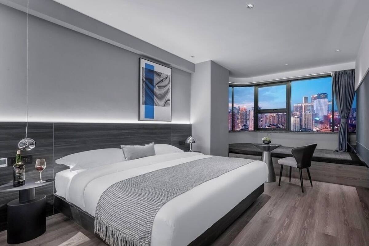 A modern hotel room with a large bed, a desk, and a view of a cityscape.