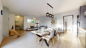 Un'area pranzo moderna con pavimento in legno, un tavolo da pranzo imbandito per quattro e una cucina con elettrodomestici in acciaio inossidabile.