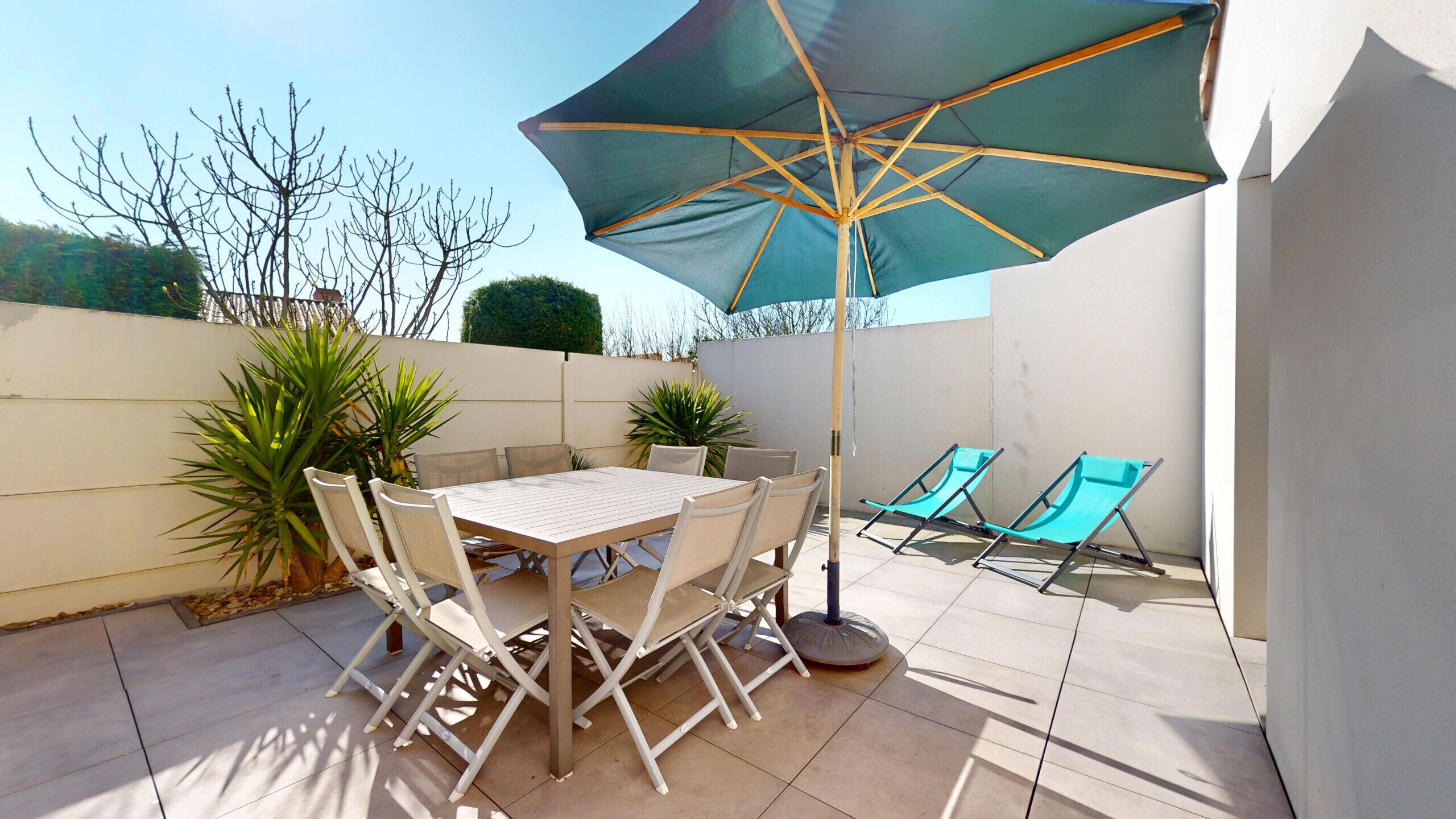 Un patio con una mesa, sillas y dos sillones de descanso, además de una sombrilla.