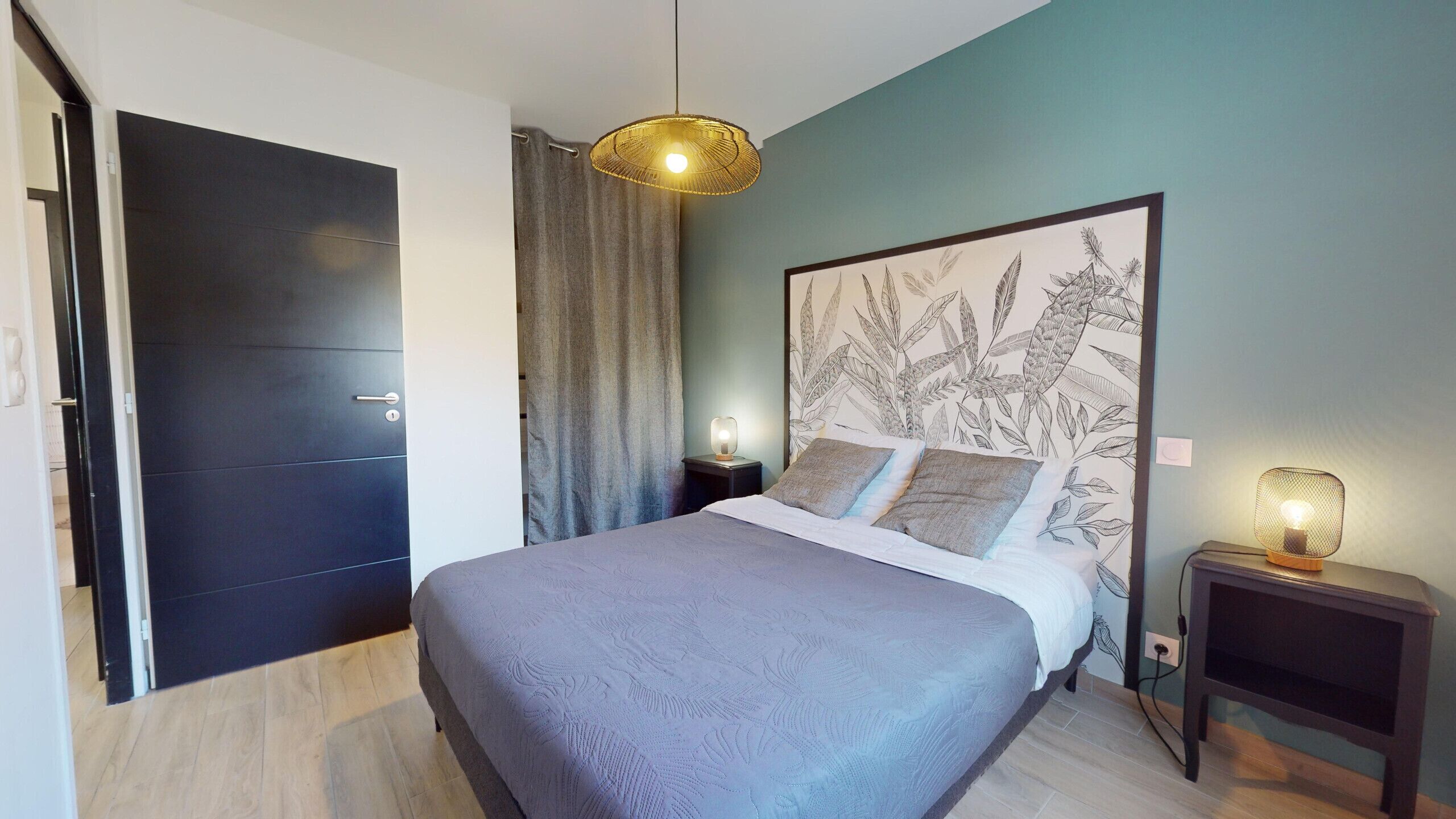 A modern bedroom with a dark door, a bed with a floral-patterned headboard, and two bedside lamps.