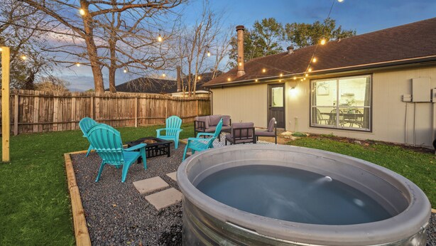 Un patio trasero con jacuzzi, mobiliario exterior e iluminación colgante.