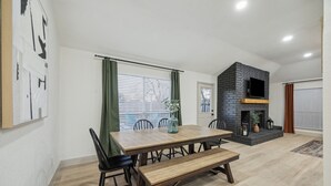 Un comedor con mesa de madera, sillas y banco. Hay una chimenea con un televisor encima.