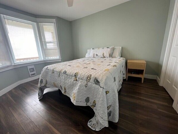 A bedroom with a bed, a nightstand, and a window with blinds.