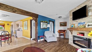 A living room with a fireplace, a television mounted on the wall, and a dining area with a table and chairs.
