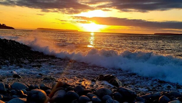 A sunset over a rocky shoreline with waves crashing onto the rocks.