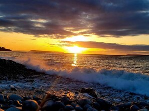 Solnedgang over en klippefyldt kystlinje med bølger der slår mod klipperne.