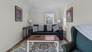 Een woonkamer met een donkere bank, een houten salontafel en gekleurde vloerkleden.