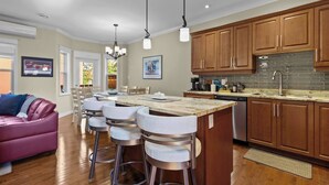 A modern kitchen with wooden cabinets, a marble countertop, and bar stools.