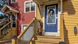 A two-story house with a front porch, wooden steps, and a blue door.