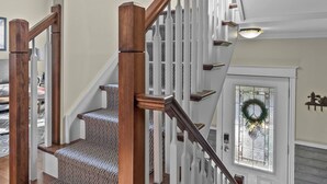 A staircase with wooden railings and patterned carpet, leading to a door with a wreath.