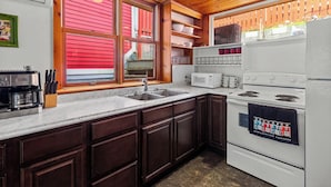 A kitchen with wooden cabinets, a white stove, a sink, and a window with red shutters.