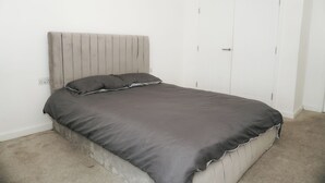 A single-bed room with a grey headboard, a grey bedspread, and a white door.