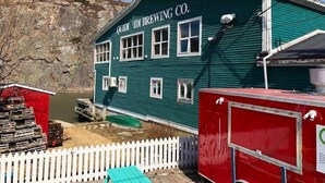 Un edificio verde con la scritta "QUIDI TID BREWING CO." sul lato, una recinzione bianca a picco e un rimorchio rosso nelle vicinanze.