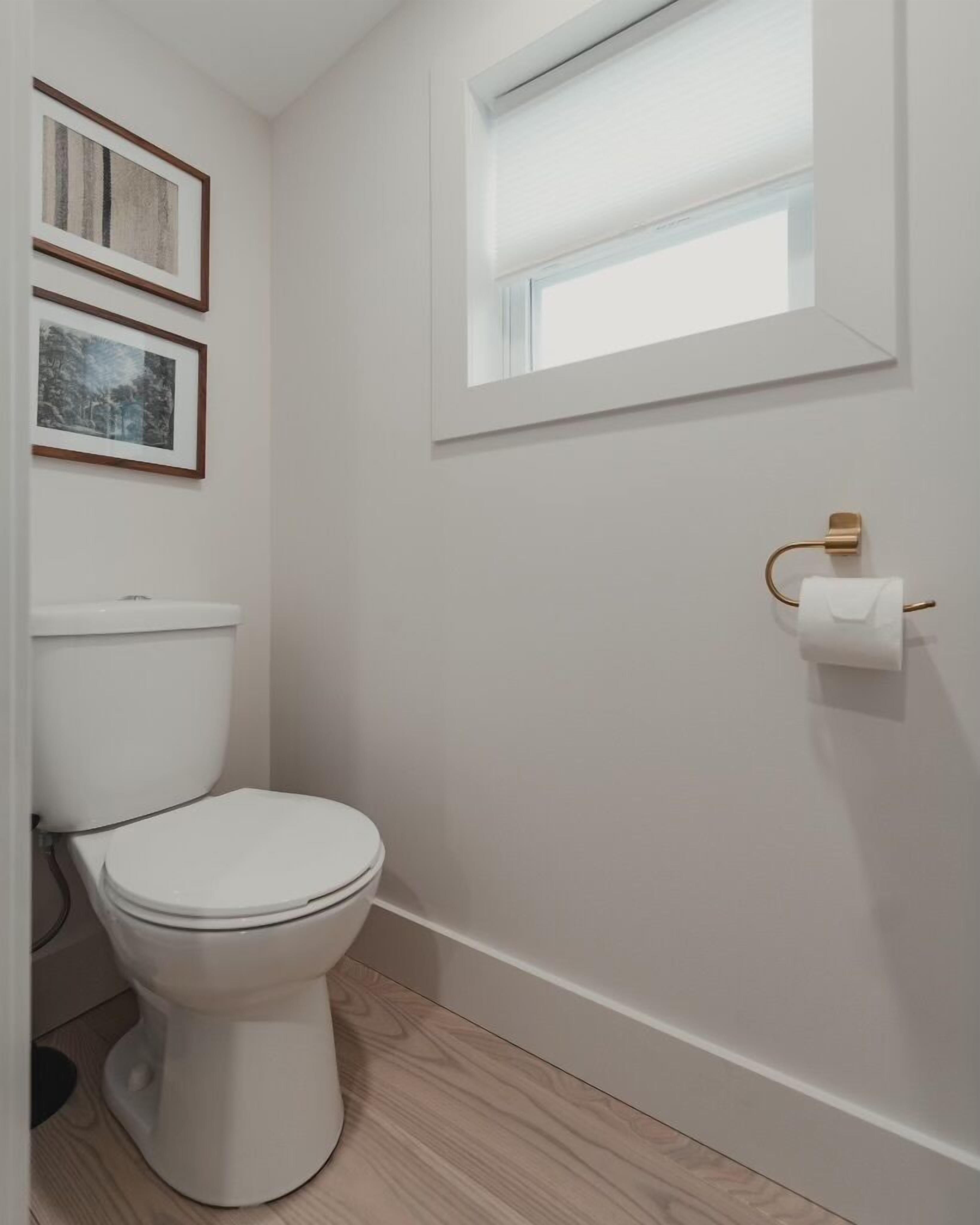 Une petite salle de bain moderne avec des toilettes blanches, un plancher en bois et une fenêtre qui laisse entrer la lumière naturelle.