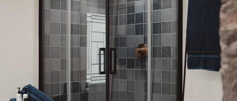 Un baño moderno con cabina de ducha de vidrio, un taburete de madera con artículos de tocador y un perchero.