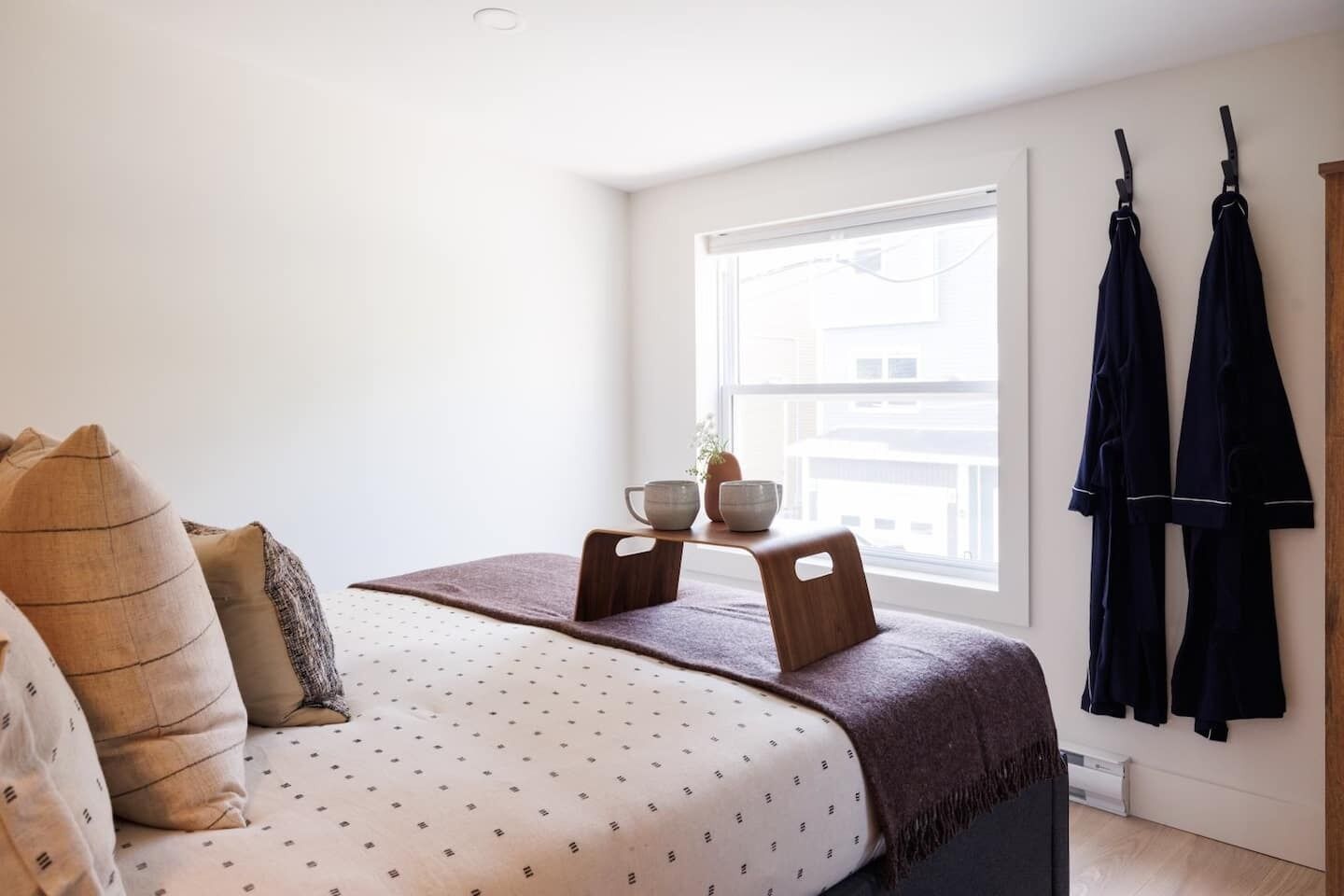 A bedroom with a bed, pillows, a bedside table with two bowls, and a window with a view of buildings.