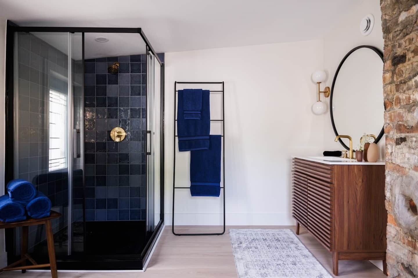 Een moderne badkamer met een douchecabine van glas, een houten wastafelmeubel met een spiegel, en een blauwe handdoekhouder.