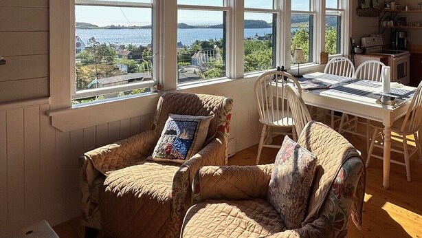 A room with large windows, a wooden ceiling, a dining table with chairs, and a cozy seating area. - Trinity's Oceanview Gem: 2BR St. Paul's Schoolhouse (Trinity)