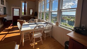 A room with a dining table, chairs, a ceiling fan, large windows with a view, and a door labeled 'Court House Road'. - Trinity's Oceanview Gem: 2BR St. Paul's Schoolhouse (Trinity)