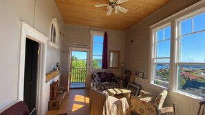 A cozy room with a wooden ceiling, large windows, a ceiling fan, and a view of the outdoors. - Trinity's Oceanview Gem: 2BR St. Paul's Schoolhouse (Trinity)