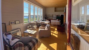 A cozy room with a wooden ceiling, large windows, a dining area, and a kitchen. - Trinity's Oceanview Gem: 2BR St. Paul's Schoolhouse (Trinity)