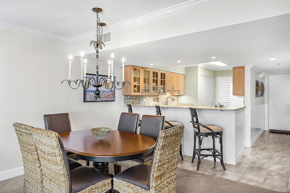 A dining area with a round table and chairs, a chandelier, and wooden cabinets in the background. - Mainsail 471 - Gulf Front Condo, Community Pool, Hot Tub, Free Beach Service! (Miramar Beach)