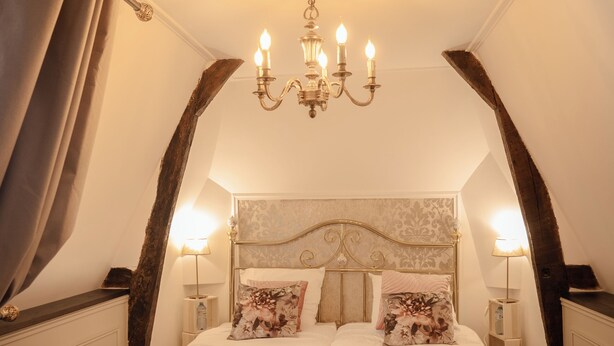 Une chambre à coucher avec un grand lit, un lustre et un banc.