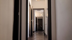 Un couloir avec un plancher en bois foncé, des murs blancs et des moulures noires. Des portes se trouvent de part et d’autre, donnant accès à d’autres pièces.