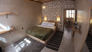 A bedroom with a stone wall, a bed with a green blanket, a wooden ceiling, and a window. - Sidi Kaouki Full Apartment Seafront  (Sidi Kaouki)