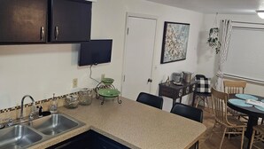Een kleine keuken met donkere kastjes, een dubbele spoelbak en een eethoek met tafel en stoelen.