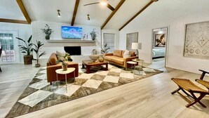 Een ruime woonkamer met een open haard, een televisie en een groot raam.