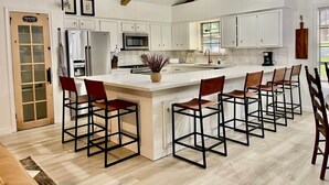 Een keuken met witte kasten, een centraal eiland met barstoelen en een houten plafond.