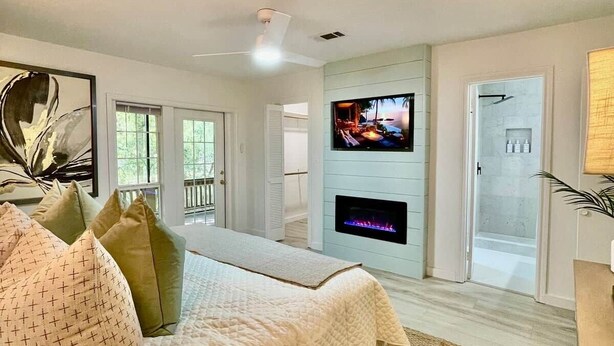 Een slaapkamer met een bed, een flatscreen-tv, een open haard en een deur naar een badkamer.