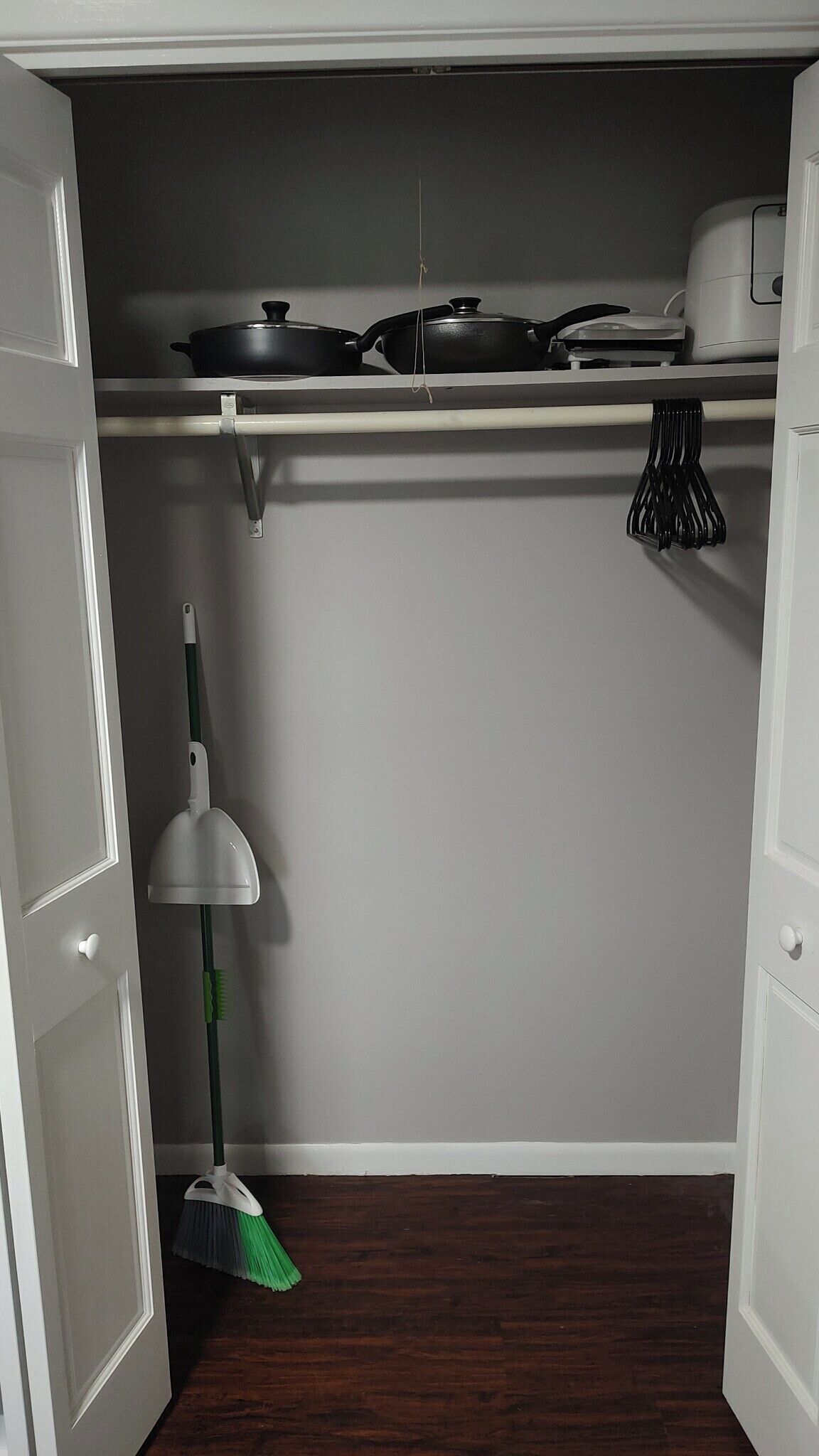 Een keuken met een fornuis, pannen en een bezem.