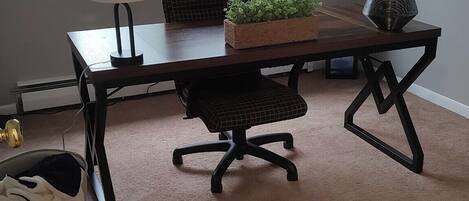 A room with a large window, a desk with a chair, a lamp, and a small plant on the desk.