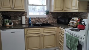 Una cocina con armarios color beige, un lavamanos negro, un microondas, una estufa y una ventana con vistas a casas.