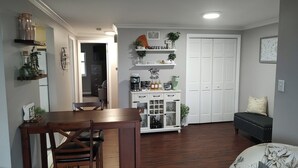 Un comedor con una mesa y sillas de madera, un armario blanco con equipo para preparar café, y una puerta cerrada al fondo.