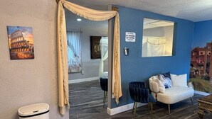 Habitación de hotel con una pared azul de acento, un sofá blanco, un espejo decorativo y un cuadro del Coliseo.