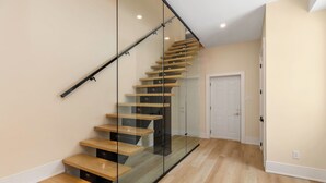 A modern staircase with glass railings and wooden steps, leading to a white door at the top.