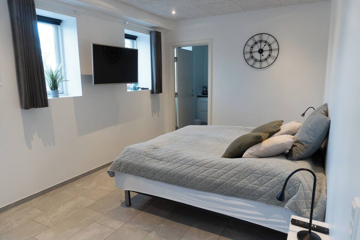 A bedroom with a bed, a TV mounted on the wall, and a clock.