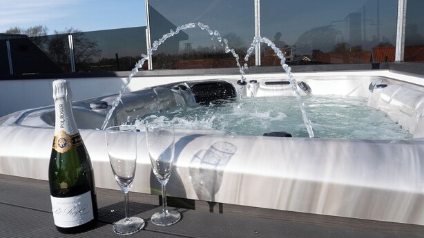Una vasca idromassaggio con getti, una bottiglia di champagne e due bicchieri su un pontile di legno.