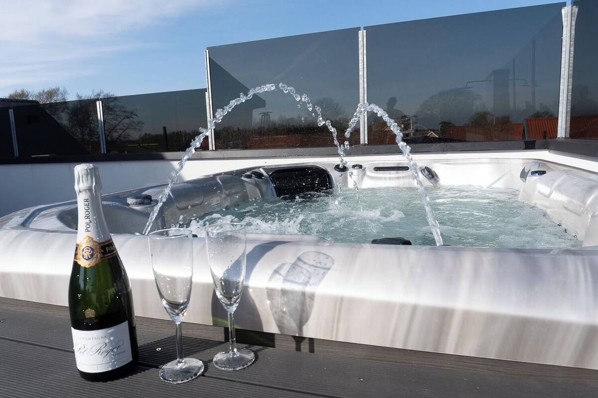 A hot tub with water jets, a bottle of champagne, and two glasses on a wooden deck.