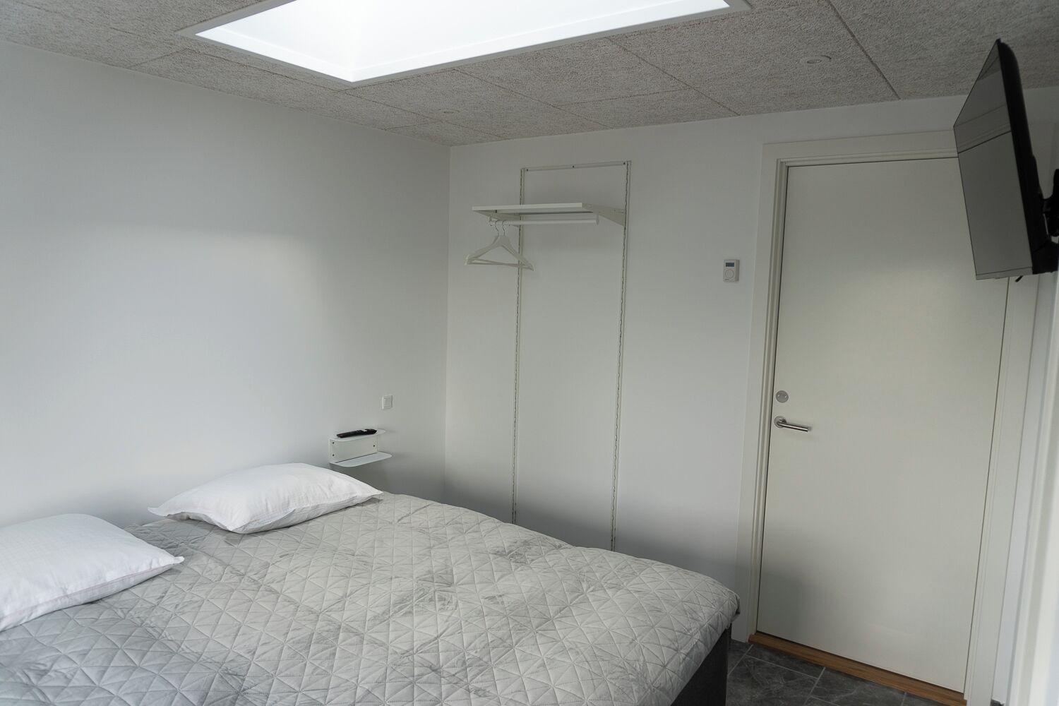 Een slaapkamer met een bed, twee kussens, een nachtkastje, een kledingkast en een plafondlamp.