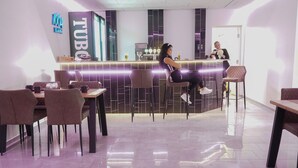 Zona bar moderna con insegna al neon, posti a sedere e pavimento lucido e riflettente.