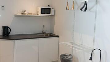 A modern kitchen with white cabinets, a black countertop, a microwave, a kettle, a sink, and a drying rack.